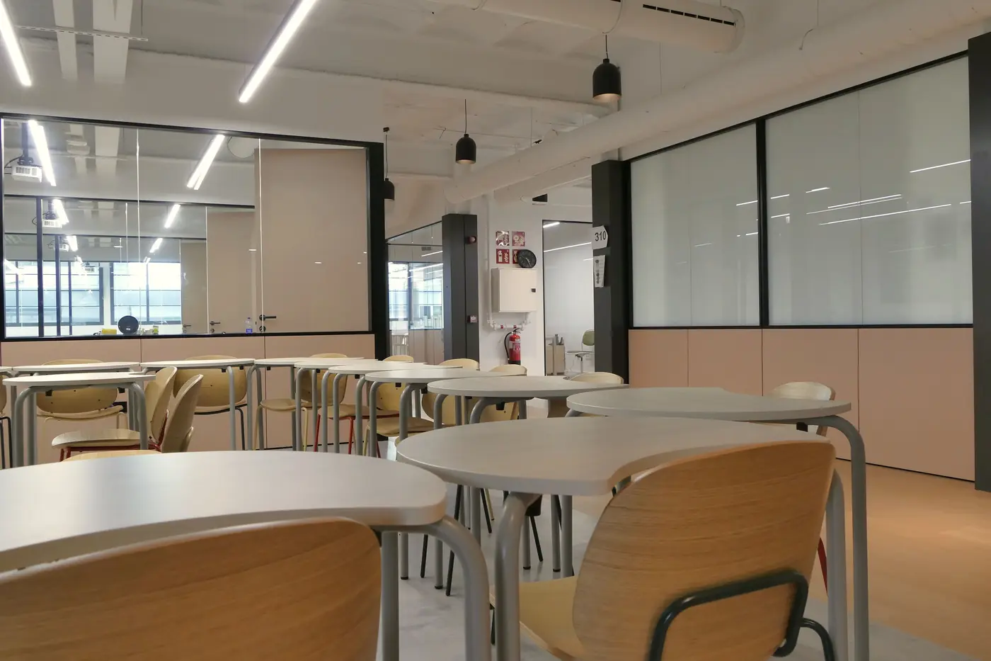 Zona común del centro educativo con mesas redondas y mamparas de vidrio.