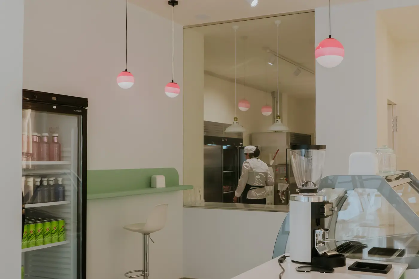 Sala de la heladería con lámparas colgantes y ventanal abierto al laboratorio.